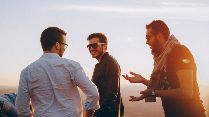 Three men talking and laughing outdoors at sunset