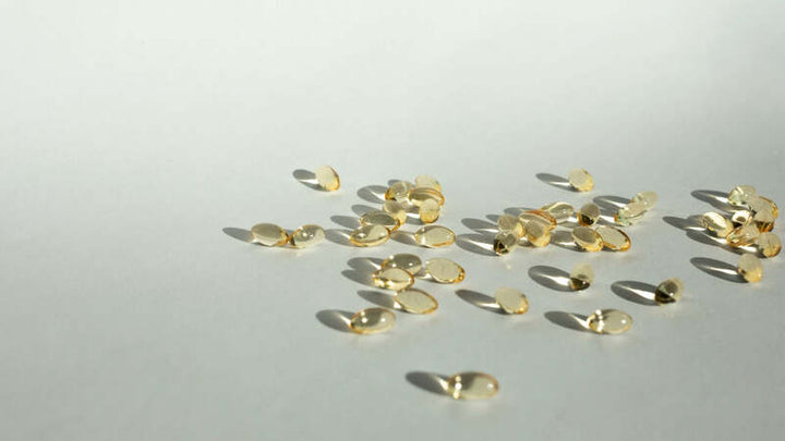Golden gel capsule supplements scattered on a light grey surface