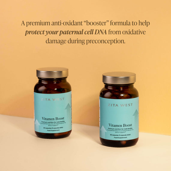 Two Zita West Vitamen Boost bottles on a cream surface against a warm golden background